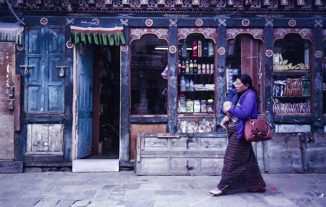 A lady hugging her baby as she walks pass a convenience store in Thimphu City, Bhutan. The colours of Bhutan are vibrant!